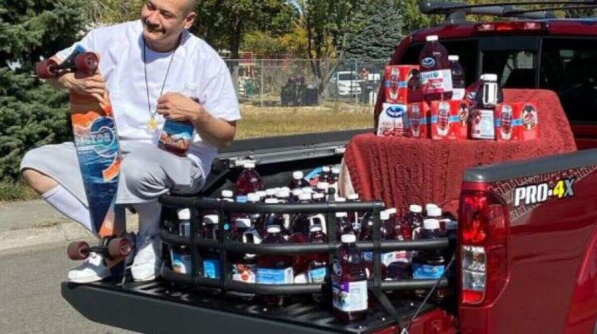 man sitting on the truck next to the drinks and holding one in his hands